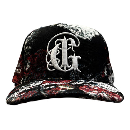 Black baseball cap with a decorative white Gothic letter and red splatter design.