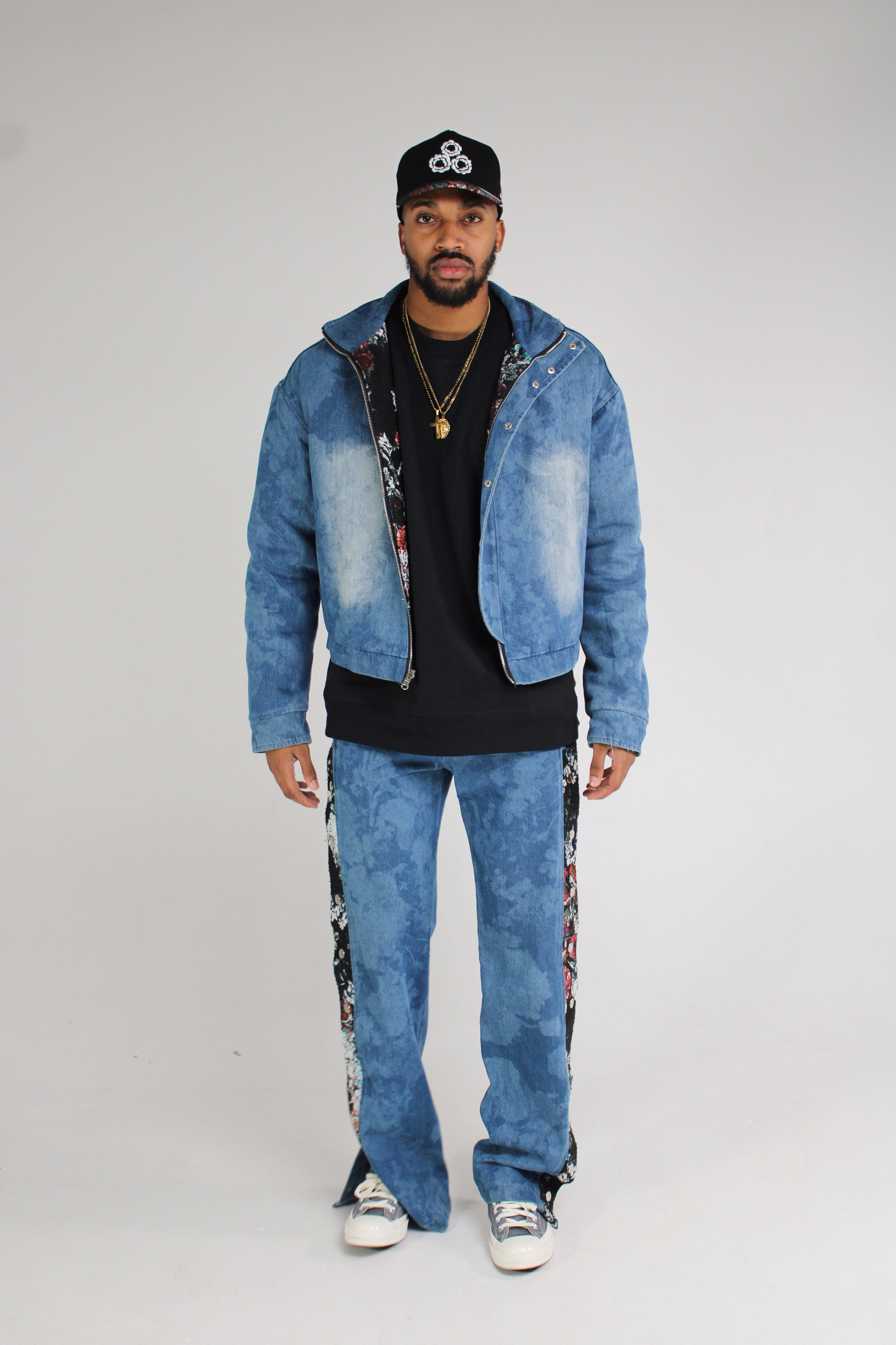 Full denim outfit with matching jacket and jeans featuring decorative embellishments, paired with a black t-shirt and baseball cap.