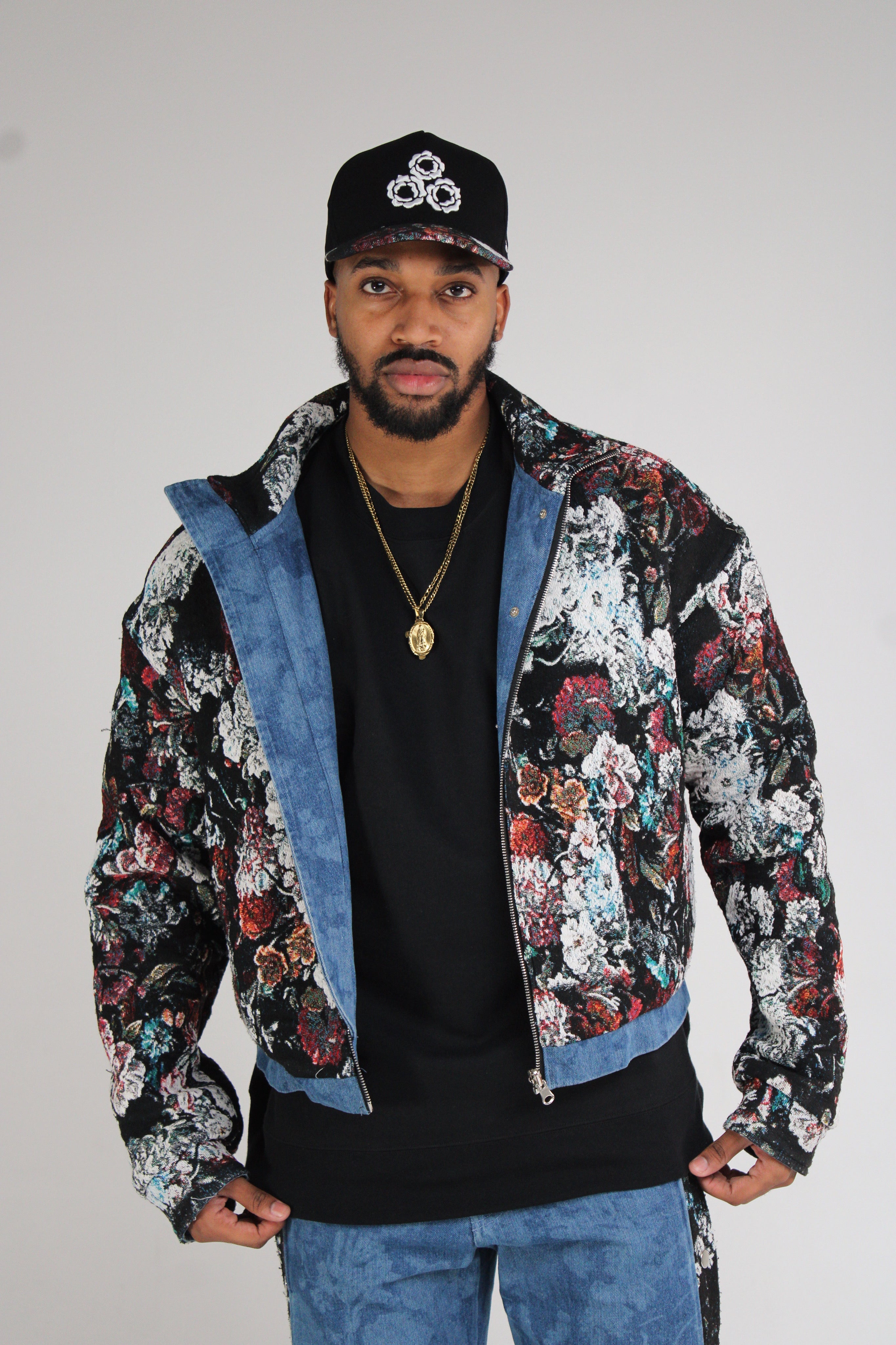 A floral patterned bomber jacket with denim accents worn over a black shirt.